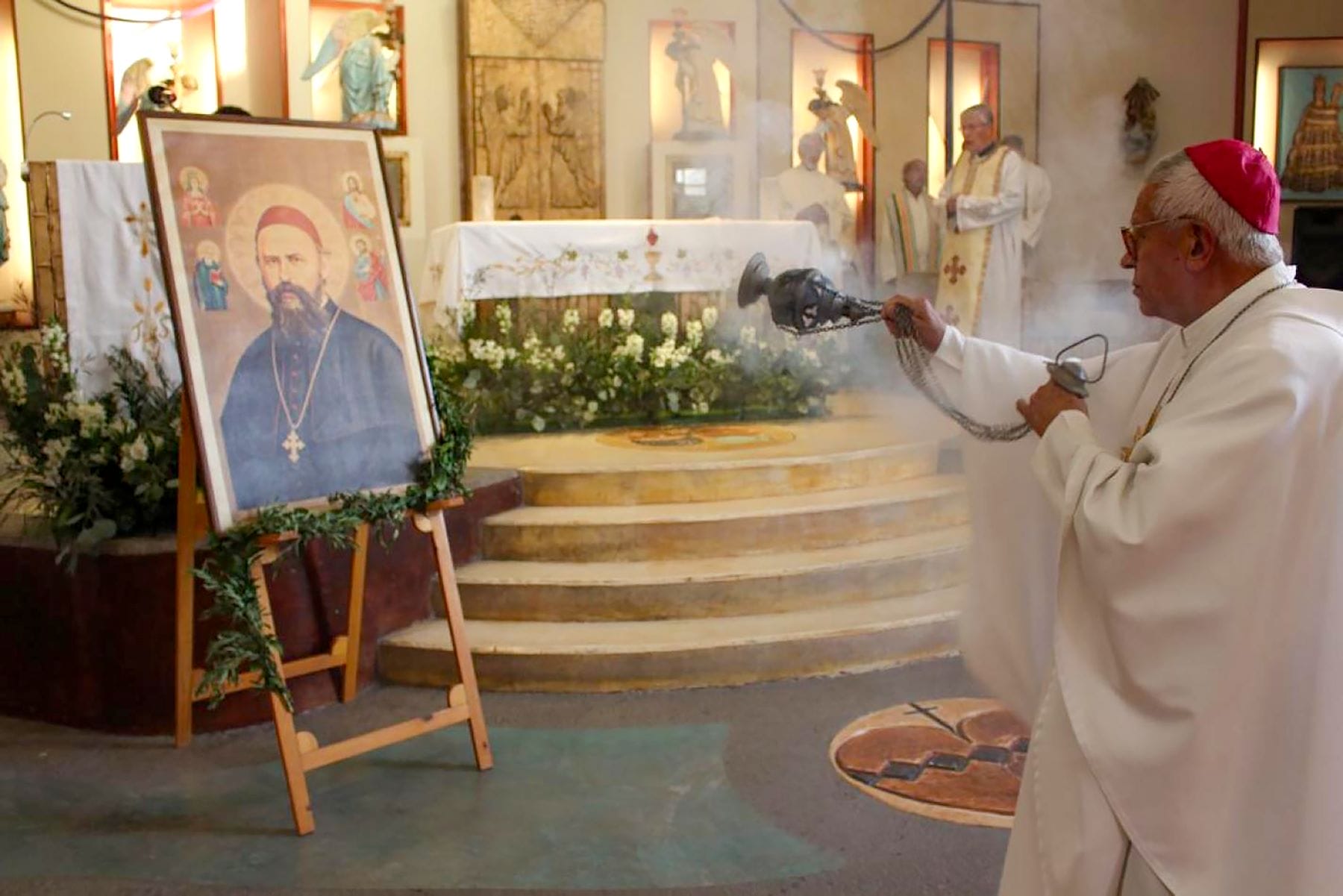 Bishop Jaime wears the traditional pink bishops cap. He is facing a portrait of St. Daniel Comboni and blessing it with incense.