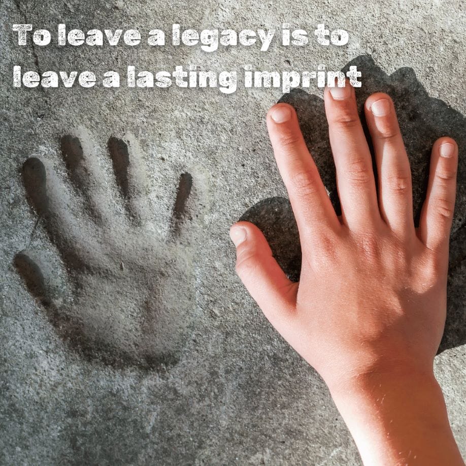 A hand rests on the ground next to a handprint pressed into concrete