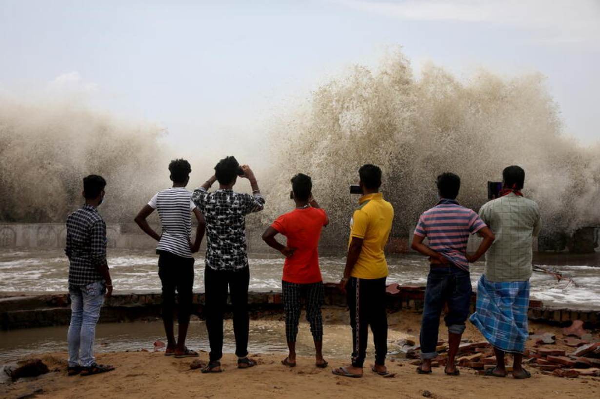 A group of young people facing away from the camera. They are using their phones to record a monsoon rains.