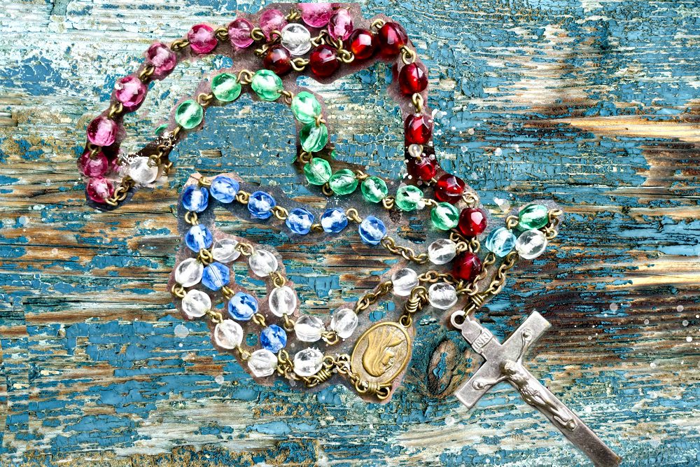 a colorful world mission rosary rests on an old wooden table with peeling paint