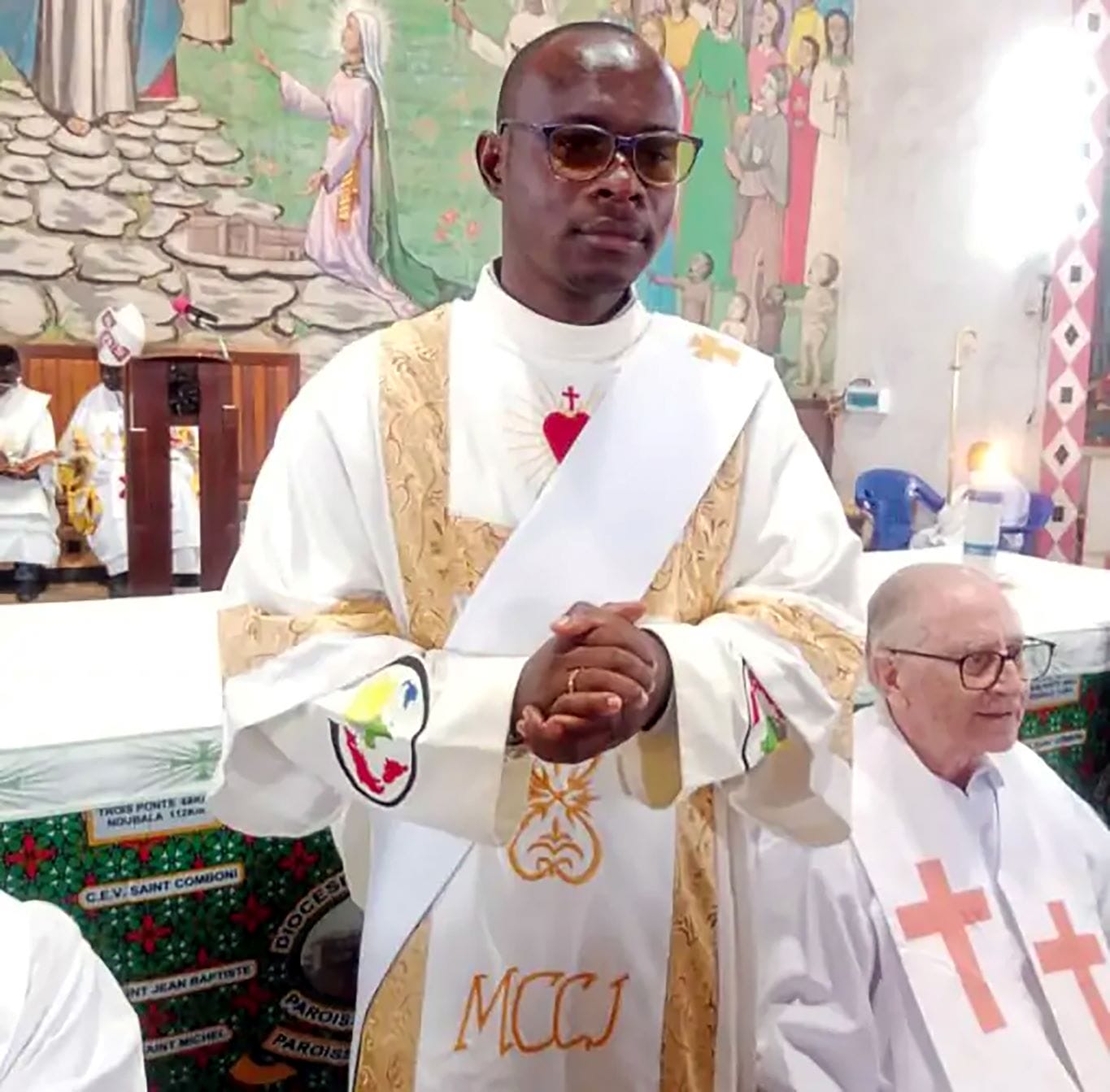 Fr Bienvenu Clemy Mikozama standing in front of an altar wearing vestments for the Sacred Heart