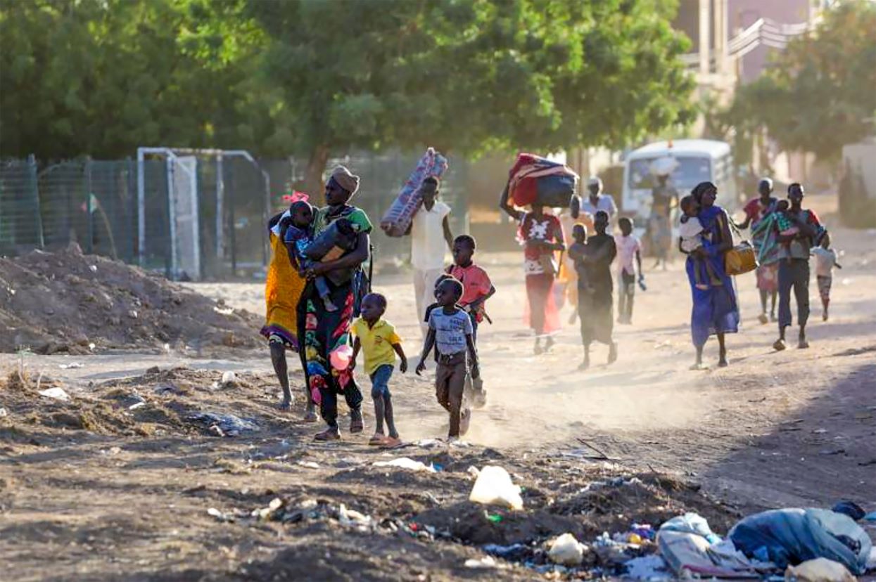 Sudanese people flee their city carrying possession on their heads down a dirt path
