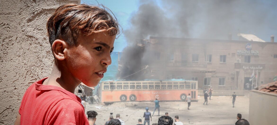 UN Middle East JPIC Young boy looks on as fighting takes place around a bus
